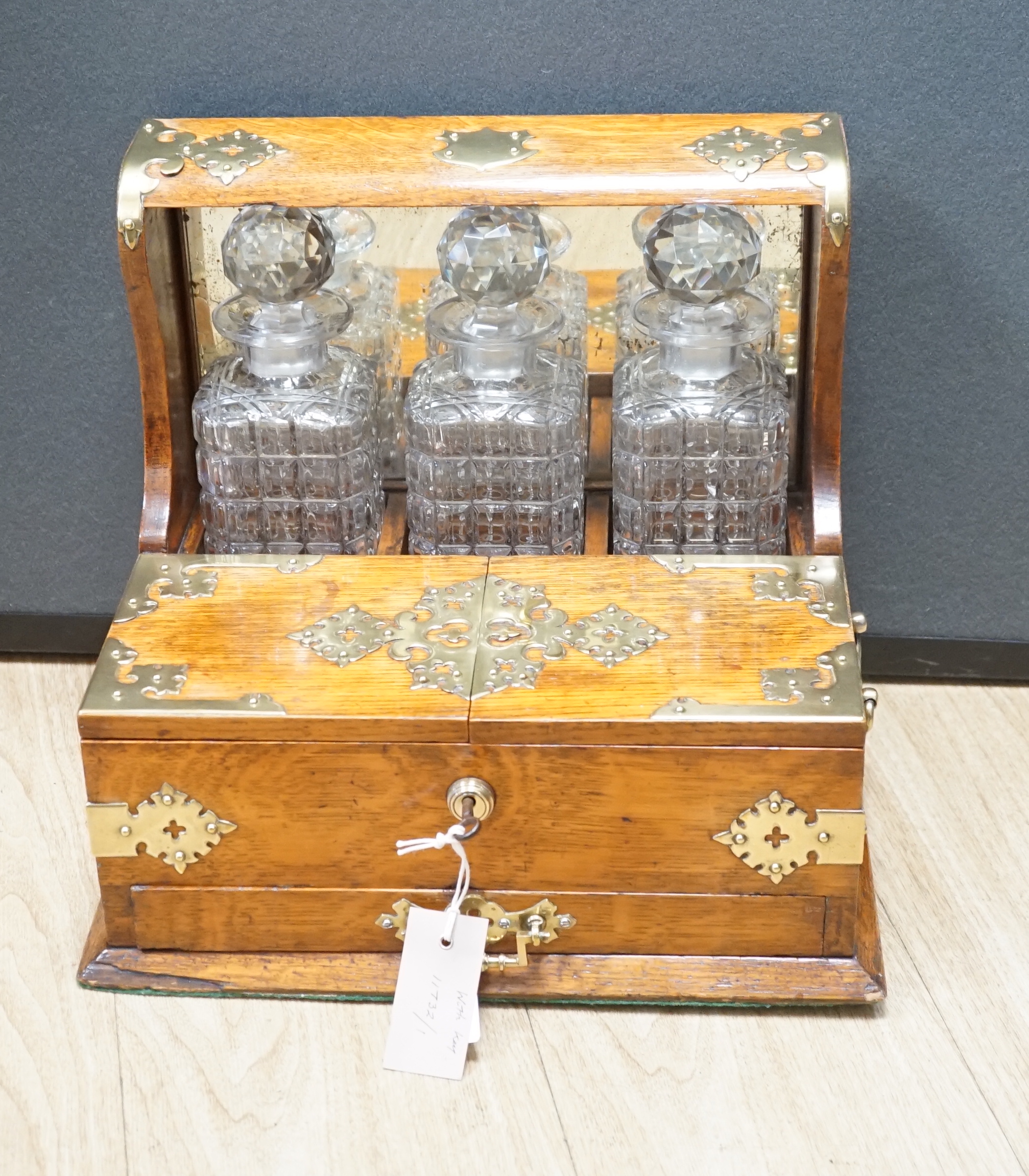 A Victorian oak and brass mounted three bottle tantalus, with base drawer and key, 36.5 cm wide